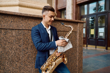 Male saxophonist poses with saxophone at building