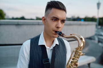 Saxophonist plays melody at the bench in city park