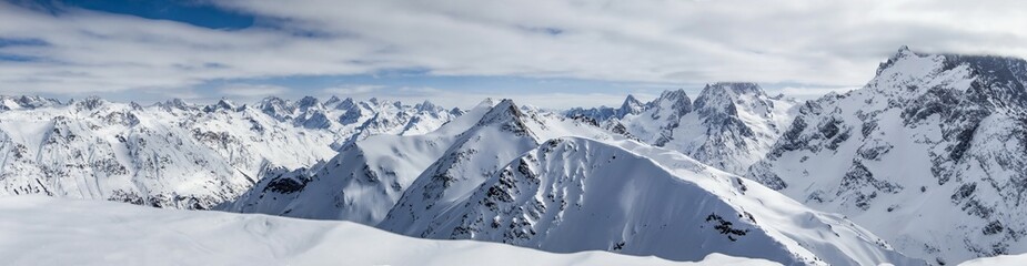 Fototapeta na wymiar Panoramic view of snowy mountains peaks in the clouds blue sky Caucasus