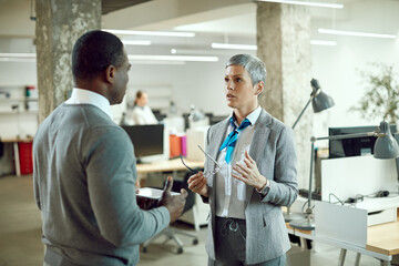 Obraz premium Female CEO talks to African American businessman during briefing at corporate office.