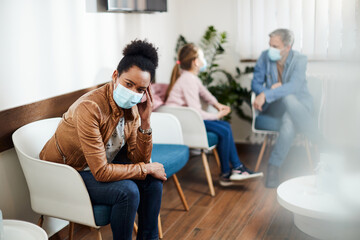 Pensive black woman wears protective face mask while waiting for dental appointment at dentist's office.