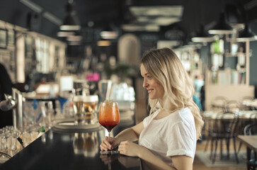 young woman at the counter of a bar drinks a cocktail