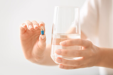 Woman with pill and water in glass on light background, closeup