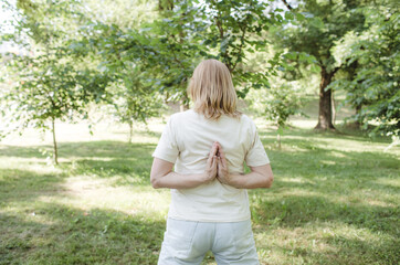 a woman does yoga in an outdoor park with her arms crossed behind her back