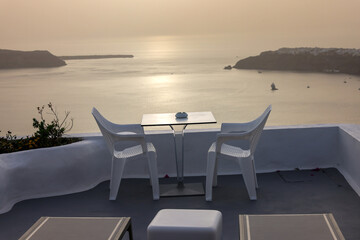 Sun loungers and chairs on terrace in the village of Imerovigli with amazing view of sunset over caldera in Santorini, Greece
