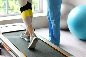 Mature physiotherapist working with young woman on treadmill in rehabilitation center