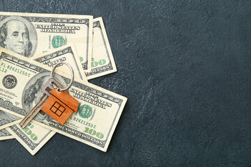 Key with wooden house shaped keychain and money on dark background