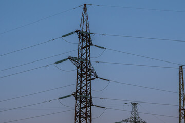 Pylons of high-voltage power lines against the background of a sunset sky. The concept of the energy crisis in Asia and Europe.