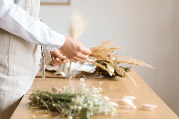 Female florist making bouquet with beautiful dried flowers at table, closeup