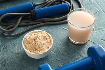 Glass of protein shake, bowl with powder, skipping rope and dumbbell on color table