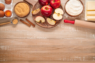Top table view on ingredients for Apple pie or Charlotte on light wooden background. Ingredients for apple pie - red apples, flour, eggs, sugar, cinnamon and butter on a wooden table