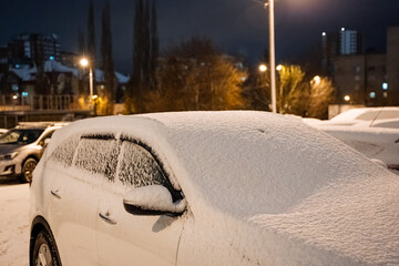 The car is covered with snow. Parking in winter. Winter frosts, street lamp shines on the car. Cleaning the machine from snow