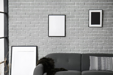 Blank picture frames and grey sofa on brick wall background