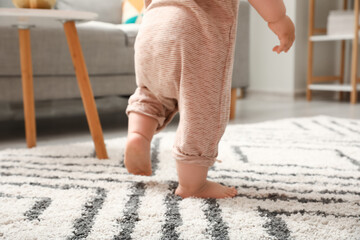 Legs of baby girl learning to walk at home, closeup