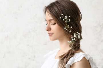 Pretty young woman with flowers in hair on light background