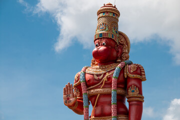 The top half of a statue of Hanuman, the Hindu god and divine vanara (monkey) companion of the god Rama, in Carapichaima on the Caribbean island of Trinidad against cloudy blue skies.