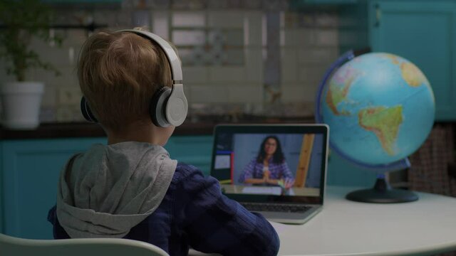 Back of online school pupil learning from home looking at laptop screen with African American female teacher talking. Kid talking to teacher using online video conference. - Powered by Adobe