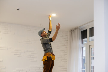 Electrician worker installation electric lamps light inside apartment. Construction decoration...