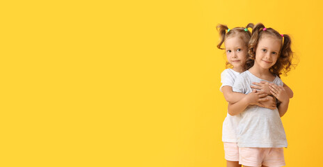 Cute little girls with ponytails hugging on yellow background - obrazy, fototapety, plakaty