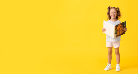 Adorable little girl with book on yellow background