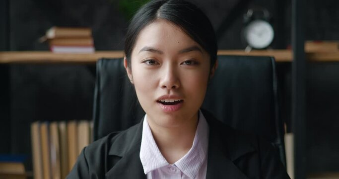 Surprised Asian business woman looks at the camera in surprise and says wow while sitting in the office. A shocked female student in formal suit rejoices at the good news, indoors