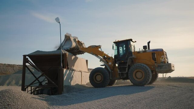 Huge wheel loader with bucket in front load stone in crusher. Heavy machinery working on quarry with equipment for production of building materials such as gravel and sand, excavator moves gravel