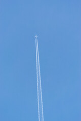 A white jet plane flies high in the blue sky and leaves behind a white trail (contrail)