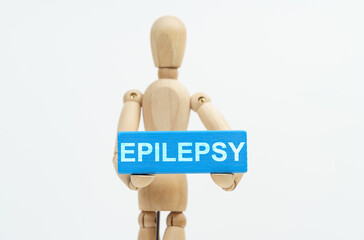 A figurine of a man holds in his hands a blue wooden block with the inscription EPILEPSY. The...
