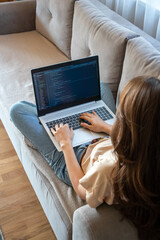 Woman working on a laptop while sitting on the sofa. A girl programmer is coding