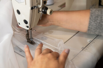 The seamstress deftly works on a sewing machine and sews white curtains. Close-up view.