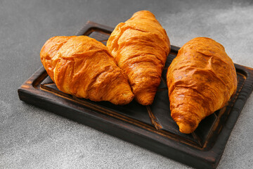 Wooden board with delicious croissants on grunge background