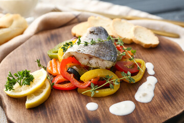 Wooden board of tasty sea bass fish with vegetables on table