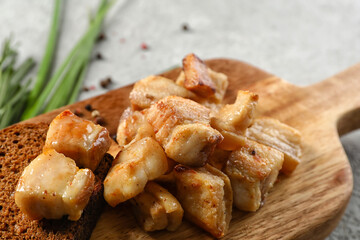 Wooden board with tasty cracklings on light background, closeup