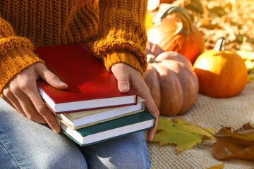 Woman holding books on warm plaid in autumn park, closeup