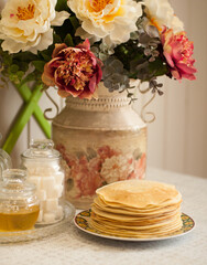 Obraz na płótnie Canvas a stack of pancakes on the background of peonies in a vase and dishes