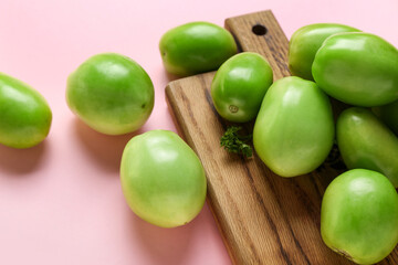 Wooden board with fresh green tomatoes on light background, closeup