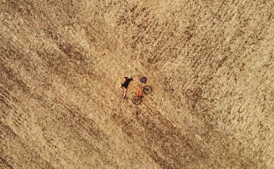 Creative aerial photo of cyclist girl lying on autumn field with orange bicycle. Minimalistic concept. Drone top view.