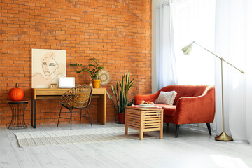Interior of light room with modern workplace and pumpkin near brick wall
