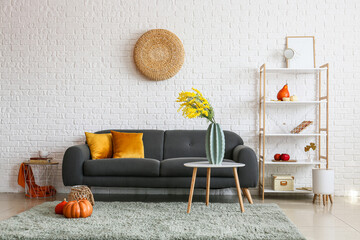 Interior of modern room with sofa, shelf unit and autumn decor near white brick wall