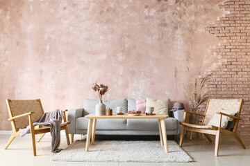 Interior of modern room with sofa, armchairs, table with bakery and cups near grunge color wall