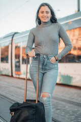 Señorita entusiasmada joven de negocios esperando en la parada del metro junto con su equipaje de mano para transportarse hasta la ciudad y comenzar su trabajo 