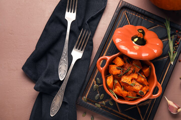 Pot with tasty roasted pumpkin on brown background