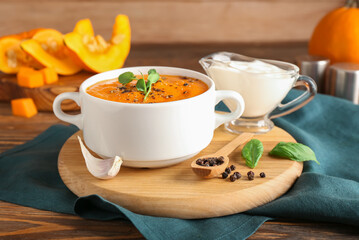 Pot with tasty pumpkin cream soup, spices and sauce on wooden background