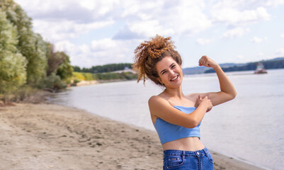 Young beautiful curly woman showing her muscles while outside