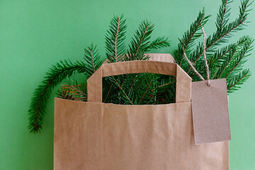 Close-up of a craft package with fir branches on a green background. An empty tag on a jute rope hangs on the branches. Copy space. The concept of New Year's gifts, Christmas surprises, Christmas sale