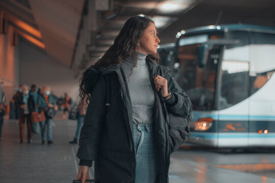 Turista de negocios de cabello oscuro observando impaciente de pie esperando con su mochila y maleta de viaje en la estaci&oacute;n de autobuses por el recinto para tomar su trayecto de transporte