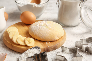 Wooden board with fresh dough and ingredients for preparing homemade cookies on light background