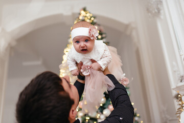 A father with a small daughter in his arms stands near the Christmas tree.