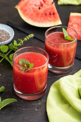 Watermelon juice with chia seeds and mint in glass on a black concrete background with green textile. Side view,  close up.