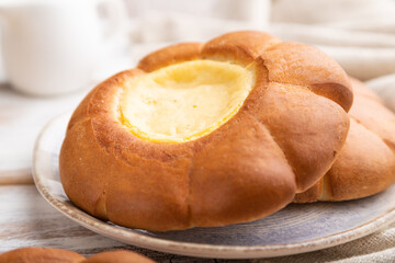Sour cream bun with cup of coffee on a white wooden background. Side view, selective focus.